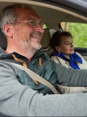 Man driving a car with a woman sitting in the passenger seat, both looking forward.