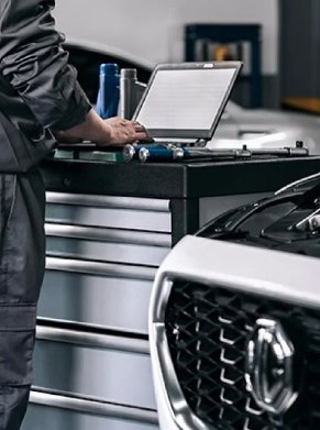 Mechanic using a laptop on a trolley beside a car with its bonnet open.