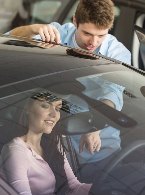 Man showing car features to woman sitting in the driver's seat.