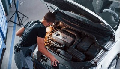 Mechanic inspecting a car engine with popped bonnet in a garage.