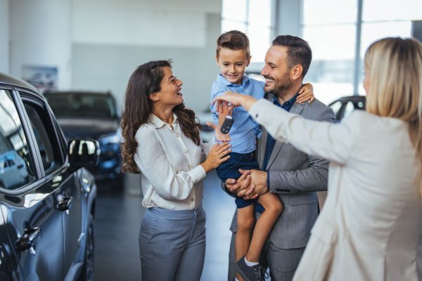 Family receiving car keys from salesperson in showroom, child holding keys while adults smile.